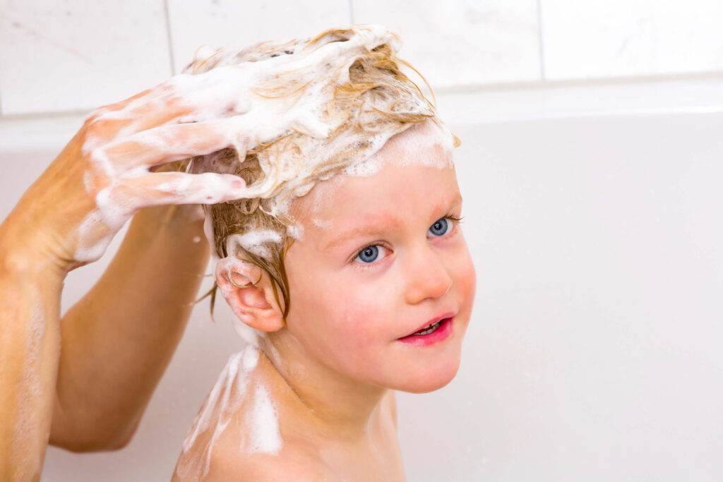 Un genitore lava i capelli del proprio figlio con uno shampoo speciale per prevenire i pidocchi del capo.